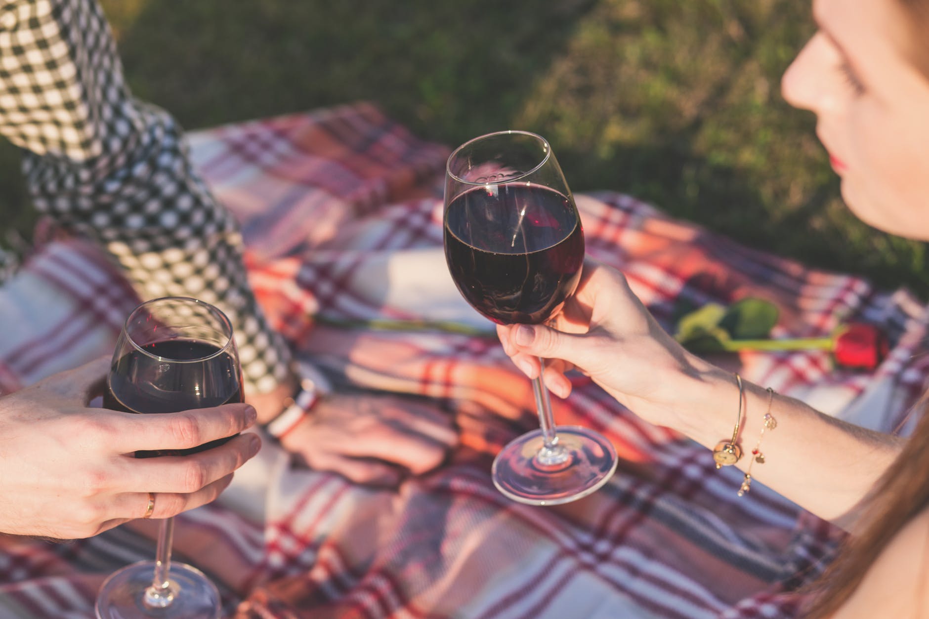 En kvinde og en made sidder udenfor på et tæppe og nyder et glas rødvin
