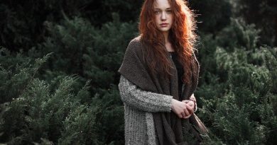 En rådhåret kvinde står med uldtøj på i en skov