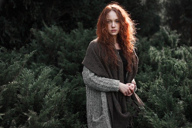 En rådhåret kvinde står med uldtøj på i en skov